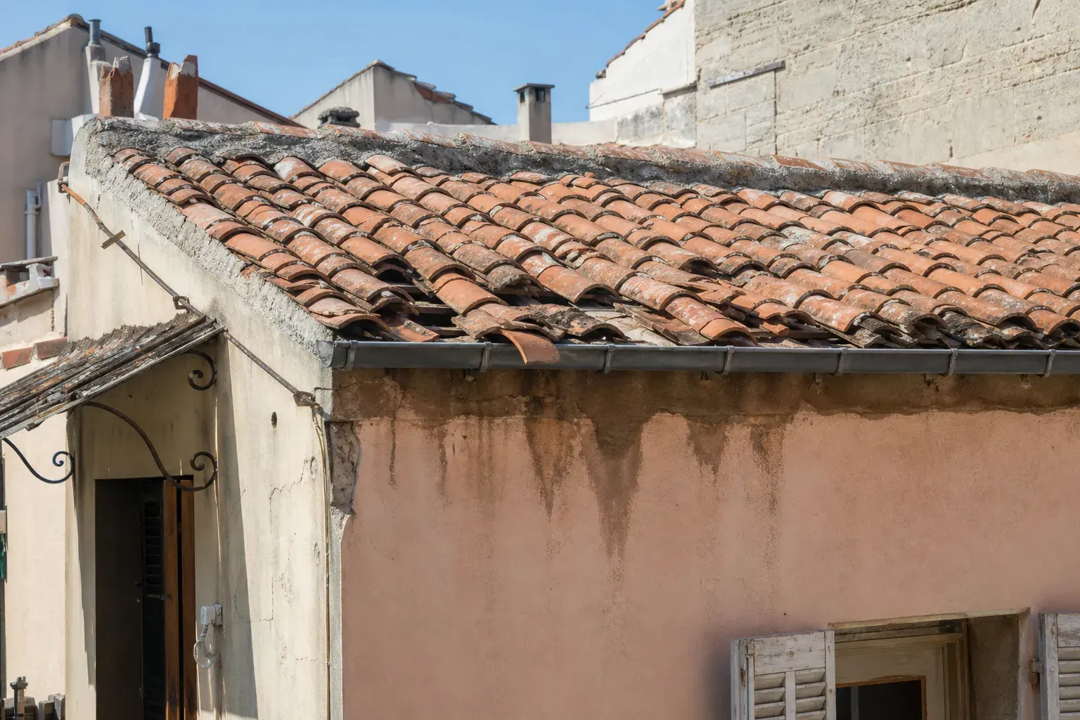 Signes de fin de vie d’une toiture réunis dans un même cadrage : rangs affaissés, tuiles glissées et brisées, auréole d’humidité sous l’égout
