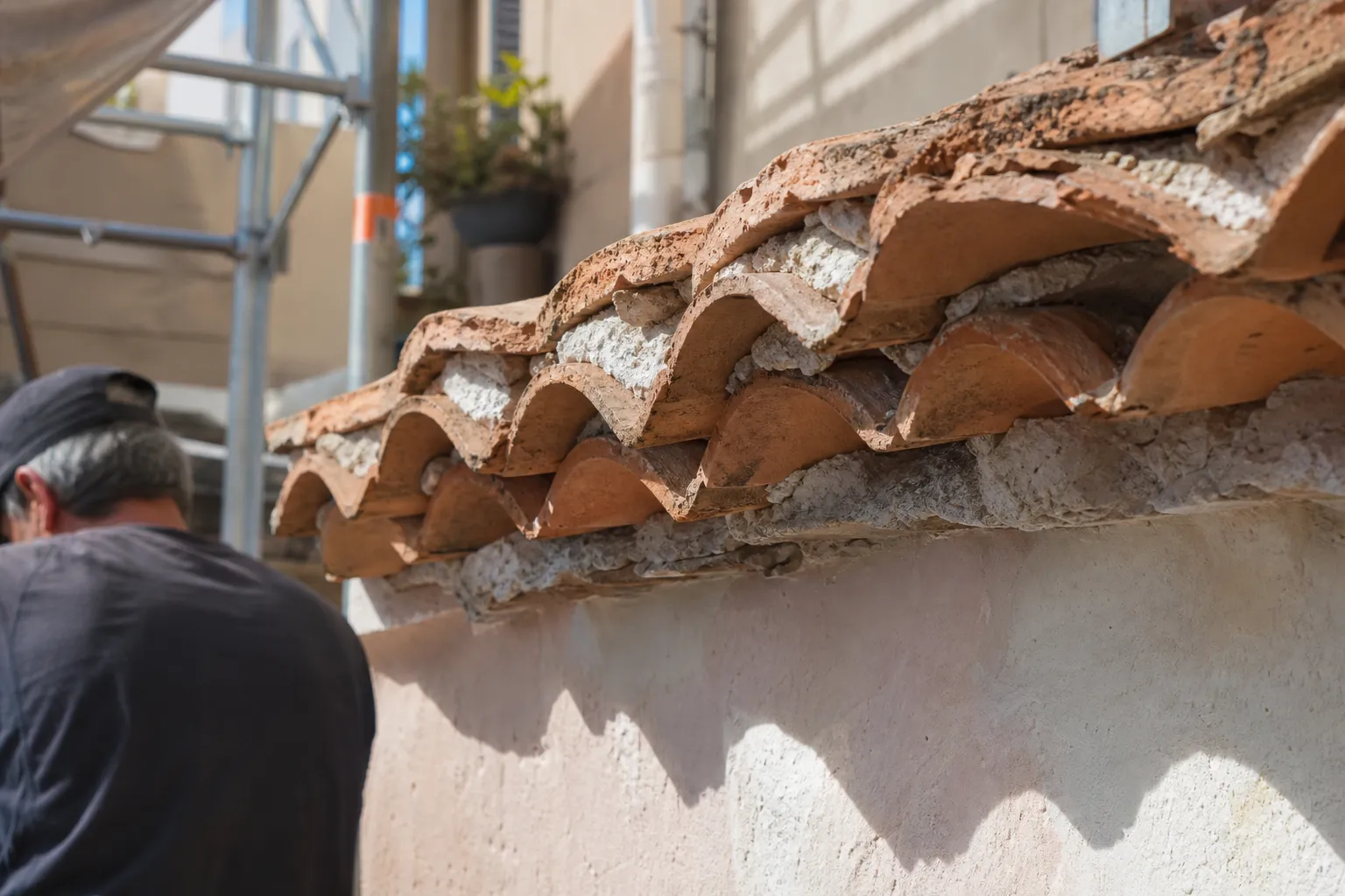 Gros plan d’une génoise provençale : trois rangs de tuiles creuses en saillie, scellés au mortier de chaux au-dessus d’un mur crème