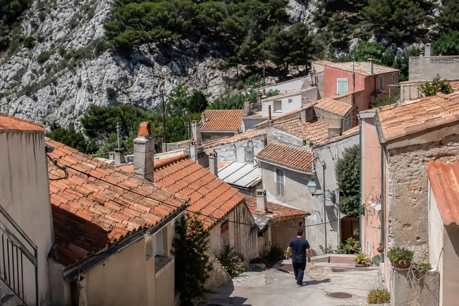 Grappe de toits bas en tuiles ocre sur un coteau au-dessus de Marseille, roche calcaire blanche et pins à l’arrière-plan