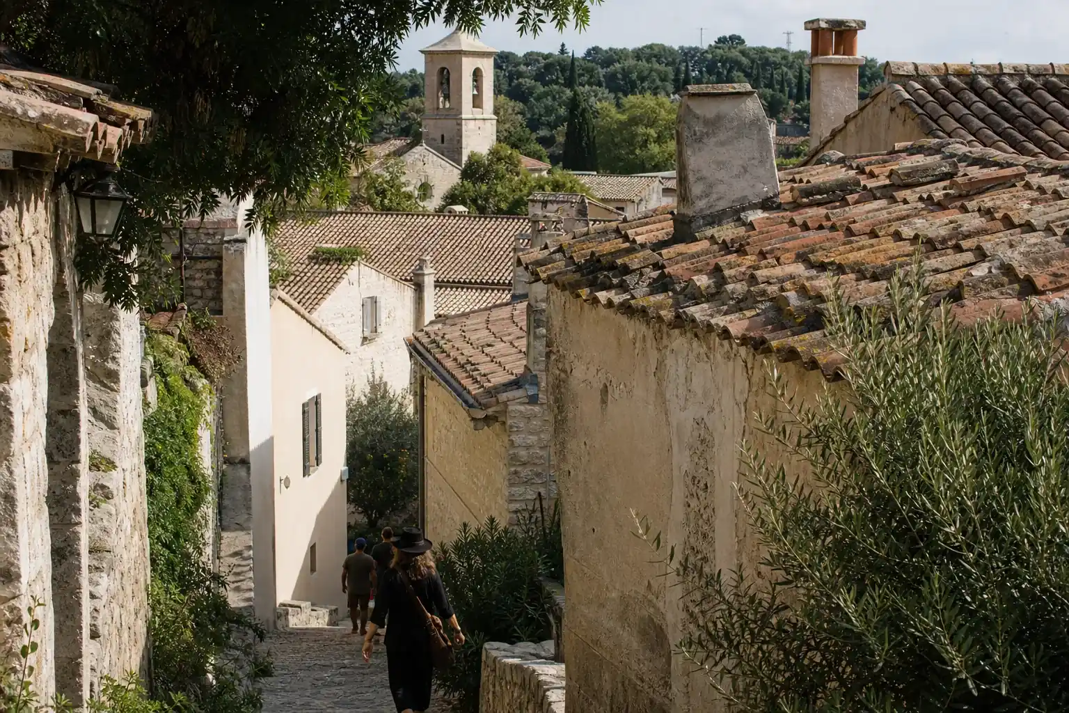Toits de tuiles d’un vieux village perché provençal vus d’une ruelle en surplomb : génoises, souches de cheminée, clocher à l’arrière