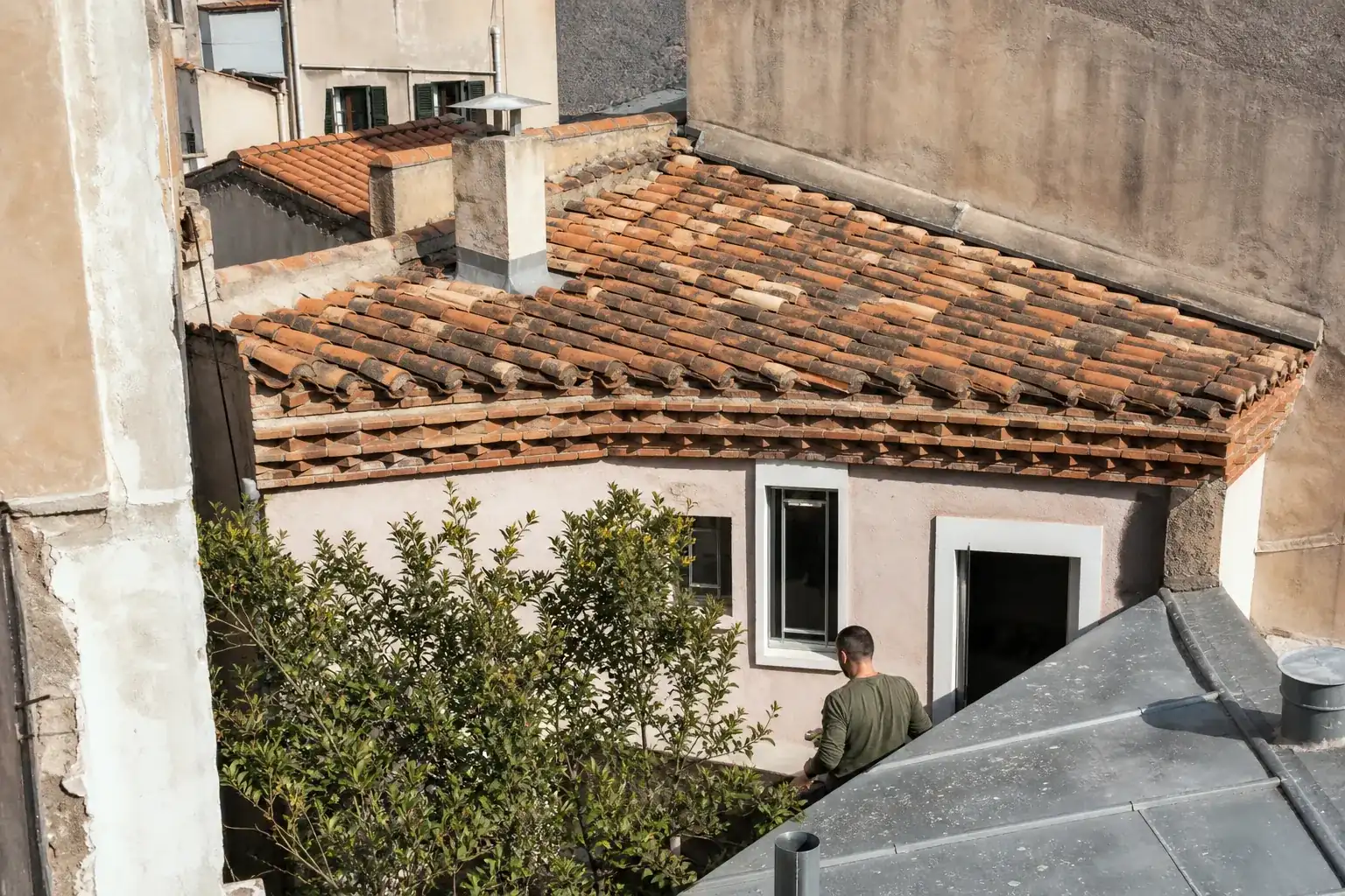 Toit d’une maison de quartier marseillaise : pente douce en tuiles creuses de terre cuite, génoise de rive en saillie, murs mitoyens de part et d’autre